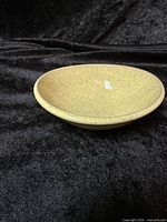 Full view of Glidden Pottery shallow bowl showing size, shape, and speckled beige glaze, placed on black fabric background.