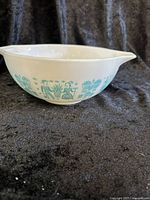 Side view of the white glass mixing bowl showing turquoise Amish Butterprint pattern of people, baskets, and wheat, with pouring spout.