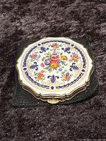 Top-down view of the round Stratton makeup compact showing detailed floral enamel design and gold-tone edges.