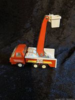 Side and angled view of the red Tonka utility bucket truck toy showing the cabin, side decals, and the boom raised with white bucket.