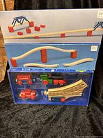Three stacked original boxes containing TC Timber wooden toy train set components including train cars, track pieces, and small supports.