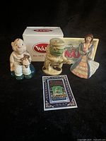 Photo of three Wade ceramic figurines in front of a white Wade box. Baby with Teddy Bear on the left, New Vic Theatre Toad of Toad Hall in center, and Belle in dress on right with certificate in foreground.