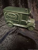 Side view of dark green ceramic vintage truck-shaped money bank with Wade Ceramics England markings.