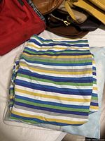 Folded striped twin sheets with blue, green, yellow, and white stripes visible, placed on bed with bags nearby.