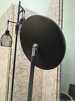 Back view of the lamp showing round weighted base and pole, and two cage-style black metal lamp shades.