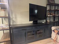 Full view of teal console table with a flat top surface, two opaque lower storage cabinets, and a middle drawer. A TV is placed on top of the table, with visible wear on the surface.
