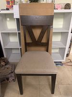 Front view of one wooden dining chair with dark brown frame and beige fabric seat, showing the V-shaped backrest design.