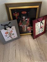 Photo of three framed Asian-themed art pieces including fabric kimono girl and two floral prints with calligraphy.