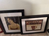 Photo showing two framed prints leaning against a wall, one jazz themed and one coffee break themed.