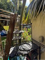 Photo showing black metal garden shelf with three tiers and nearby garden environment