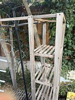 Side view showing the wooden slatted shelves and black metal hooks on top of the garden stand.