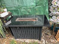 Fire pit showing black glass top with central rectangular fireburn area and black metal base with ventilation slots.