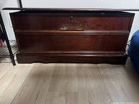 Front view of dark wood hope chest with decorative carved panel and keyhole.