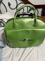 Front view of the green leather laptop bag showing handles, front flap pocket with buckle and top carrying handle.