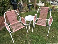 View of two pink string chairs and small round white table in garden setting