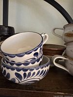 Three stacked white ceramic cups with blue leaf and heart painted motif and handles
