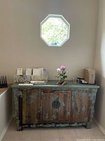 Vintage painted hardwood console under octagon window in light filled room.