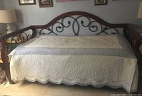 Wrought iron daybed with wooden top rail and ornate scrollwork, covered with quilted blanket, no mattress visible.