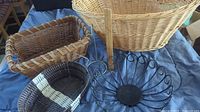 Five baskets and black metal fruit hanger displayed on a blue cloth surface showing variety in styles and colors.