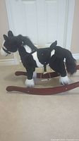 Side angle showing full body of the black and white rocking horse on wooden rockers, plush texture and details.