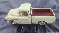 White diecast 1955 Chevrolet pickup showing side profile, truck bed with red interior, tires with chrome hubs.