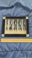 Stained glass framed picture laying flat with a ruler beside it to show size. The image depicts ballet pointe shoes in various positions in grayscale.