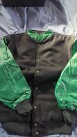 Front view of jacket with black Melton fabric body and green leather sleeves.