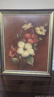 Framed floral painting with multiple flowers in warm tones on a brown background.
