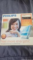 Front of the Philips goLITE BLU energy light box showing the device, a smiling woman, and product benefits.
