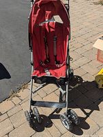 Front view of red Cosatto stroller with harness, seat, frame and wheels visible.
