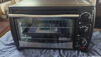 Front view of black Bravetti toaster oven showing glass door, silver handle, and three control knobs.