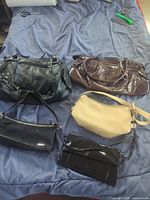 Photo showing five purses and handbags laid on a blue surface including black, brown, and beige colors of varying sizes and styles.