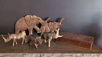 Full view of six wooden animal carvings and a vintage wooden storage/playing card box with sliding lid, all displayed on a wooden surface against a gray wall.