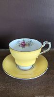 Side view of yellow Paragon teacup and matching saucer showing gold rim and handle detail