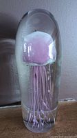 Front view showing detail of pink-purple jellyfish inside clear glass paperweight with tentacles visible.