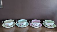 Group photo showing all four Hammersley & Co. pastel floral teacups and saucers in yellow, blue, pink, and green with gold trim on a brown surface.