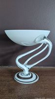 Side view showing white bowl elevated on clear swirling glass stem and round base with white accent rings.