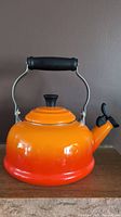 Front view of Le Creuset flame orange to red gradient kettle showing black handle and lid knob
