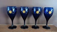 Four cobalt blue wine glasses evenly spaced in a row showing gold sun designs on the bowls.