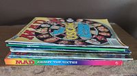 Stacked view of the ten Mad Magazines and the 'Mad About The Sixties' book in a pile showing their spines.
