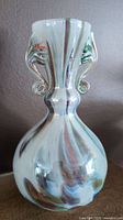 Front side close-up of the clear blown glass vase with double curled handles and swirling patterns.