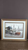 Framed oil painting on canvas featuring fishing boats in a harbour with wooden dock and building.