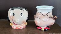 Front view of Popeye and Olive Oyl character mugs showing facial details and paint.