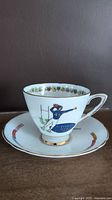 Side view of white bone china teacup on saucer showing football player design and gold rims