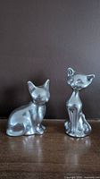 Photo of both aluminum cat sculptures side by side showing their size difference and smooth polished finish.