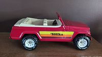 Side view showing red pressed steel body, white plastic interior, Tonka branding on yellow stripe, and Max-Trax tires.