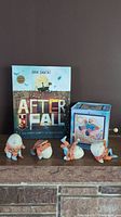 Photo of four 3-inch Humpty Dumpty porcelain figurines, the Jack-in-the-box musical toy, and the signed book "After the Fall" standing upright behind them.