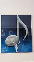 Front view of metal framed vintage print showing large musical note and conductor figure with blue background, hung on wall.