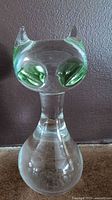 Clear glass cat figurine with green eyes on a dark background.