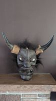 Front view of the vintage wood carved demon mask showing horns wrapped with rope, sharp facial features, and white shell eyes against a dark background.
